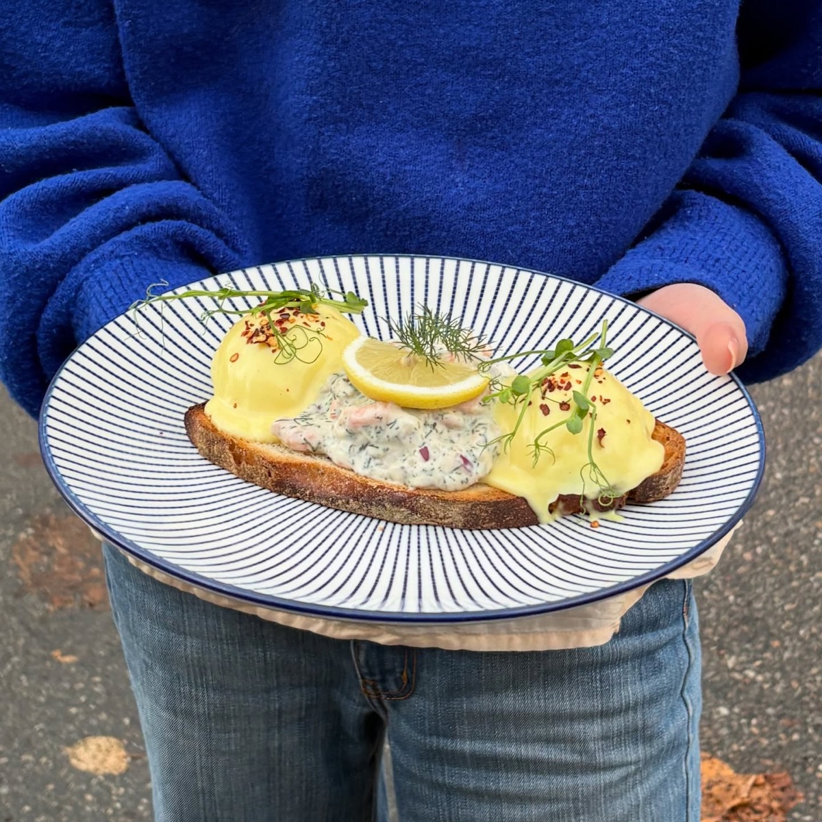 Scandi benedict med räkröra, dill och citron på en blå- och vitrandig tallrik