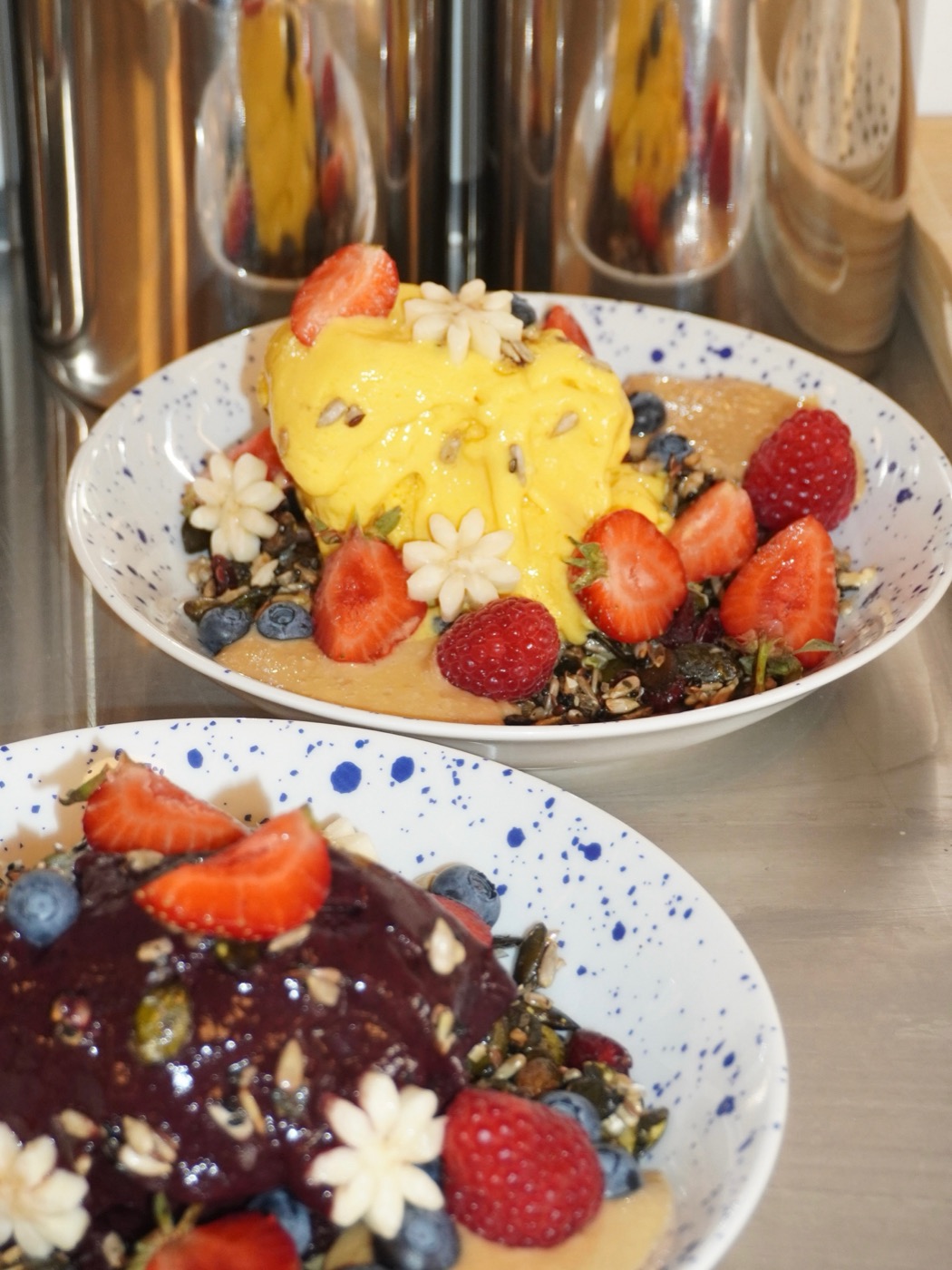 Frozen mangoyoghurt och açaí-bowl med jordgubbar, hallon och granola på prickiga tallrikar