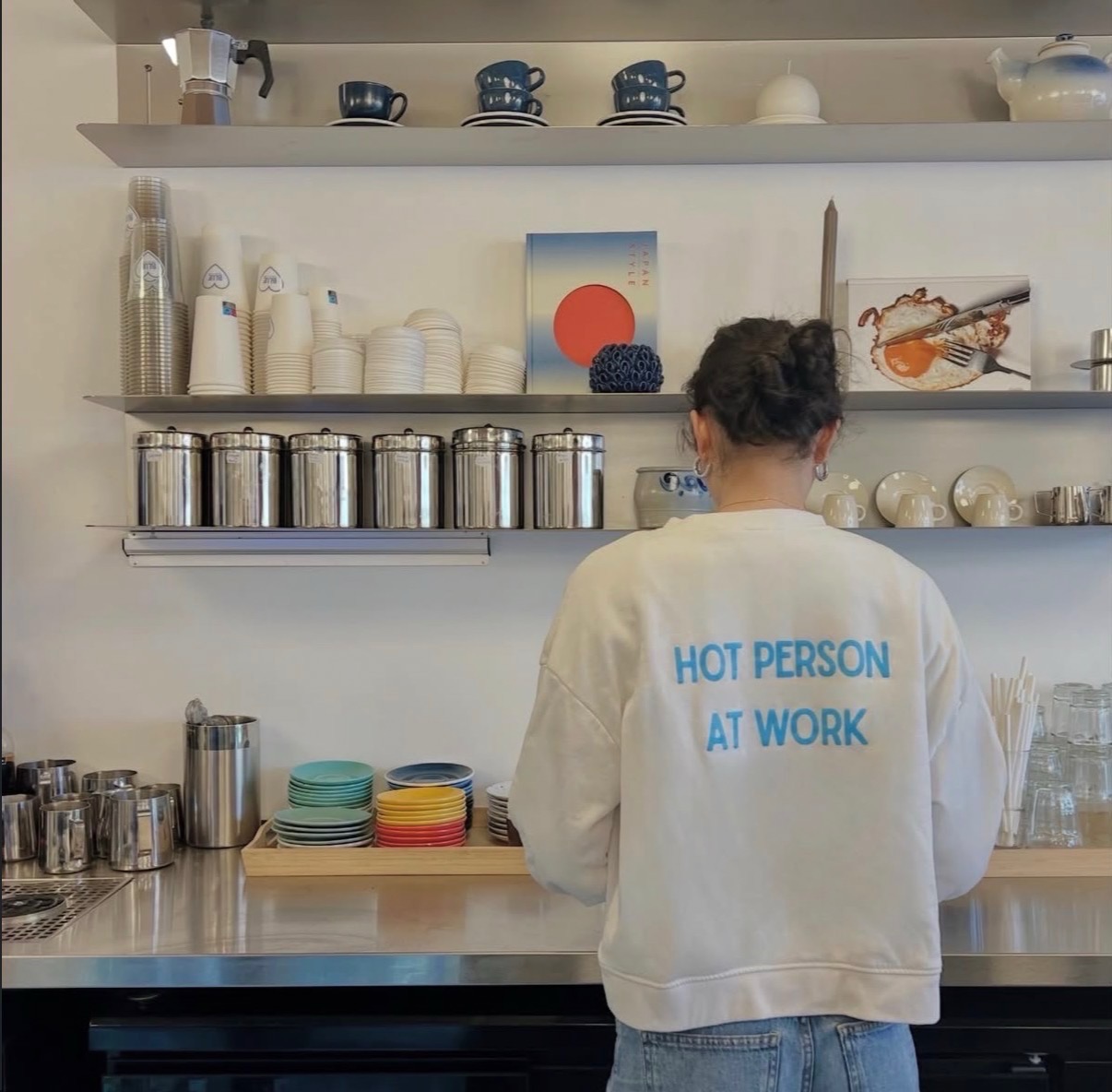 Bakom disken på Blue: hyllor med blå koppar, stålburkar och personal i vit tröja med trycket Hot person at work