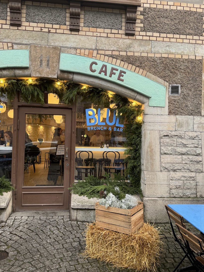 Entrén till Blue i kvällsljus med granris, ljusslinga och den turkosa Café-skylten