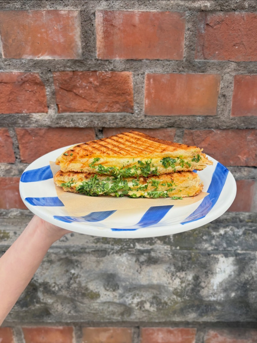 Grilled cheese med persilja på randig tallrik mot en tegelvägg
