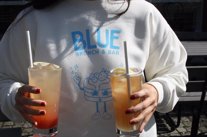 Vit tröja med trycket BLUE Brunch & Bar och två lemonader i händerna
