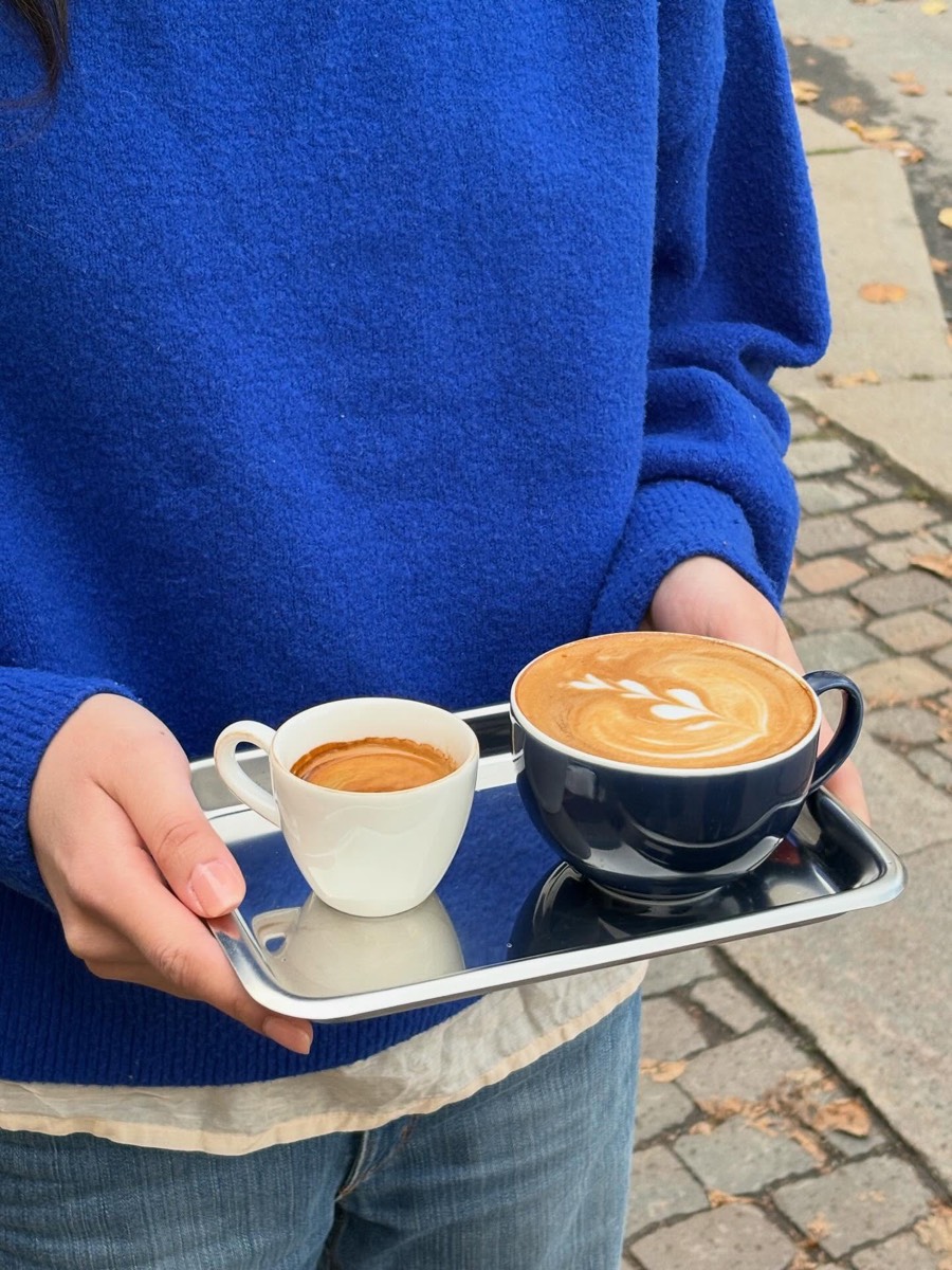 Espresso och latte på stålbricka, buren av någon i koboltblå tröja