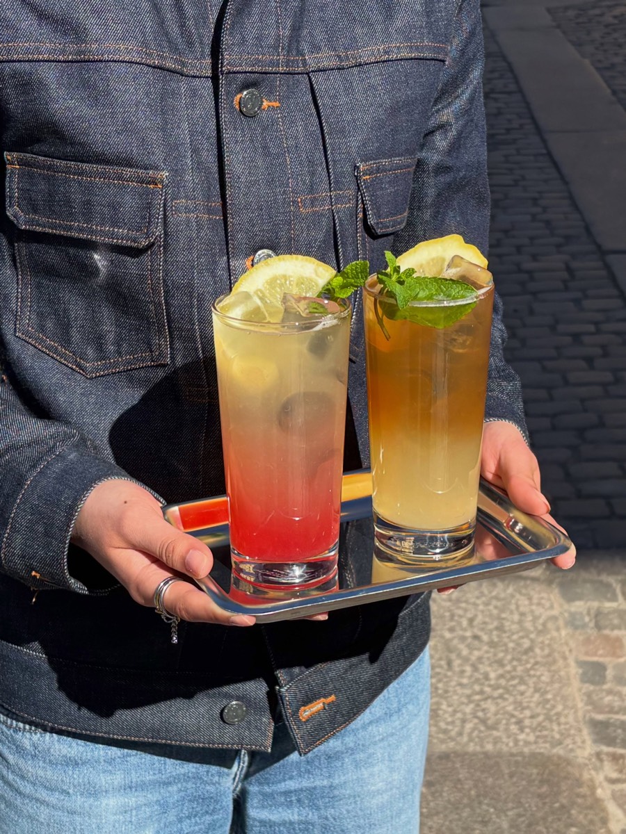Två lemonader med citron och mynta på en stålbricka, buren av någon i jeansjacka