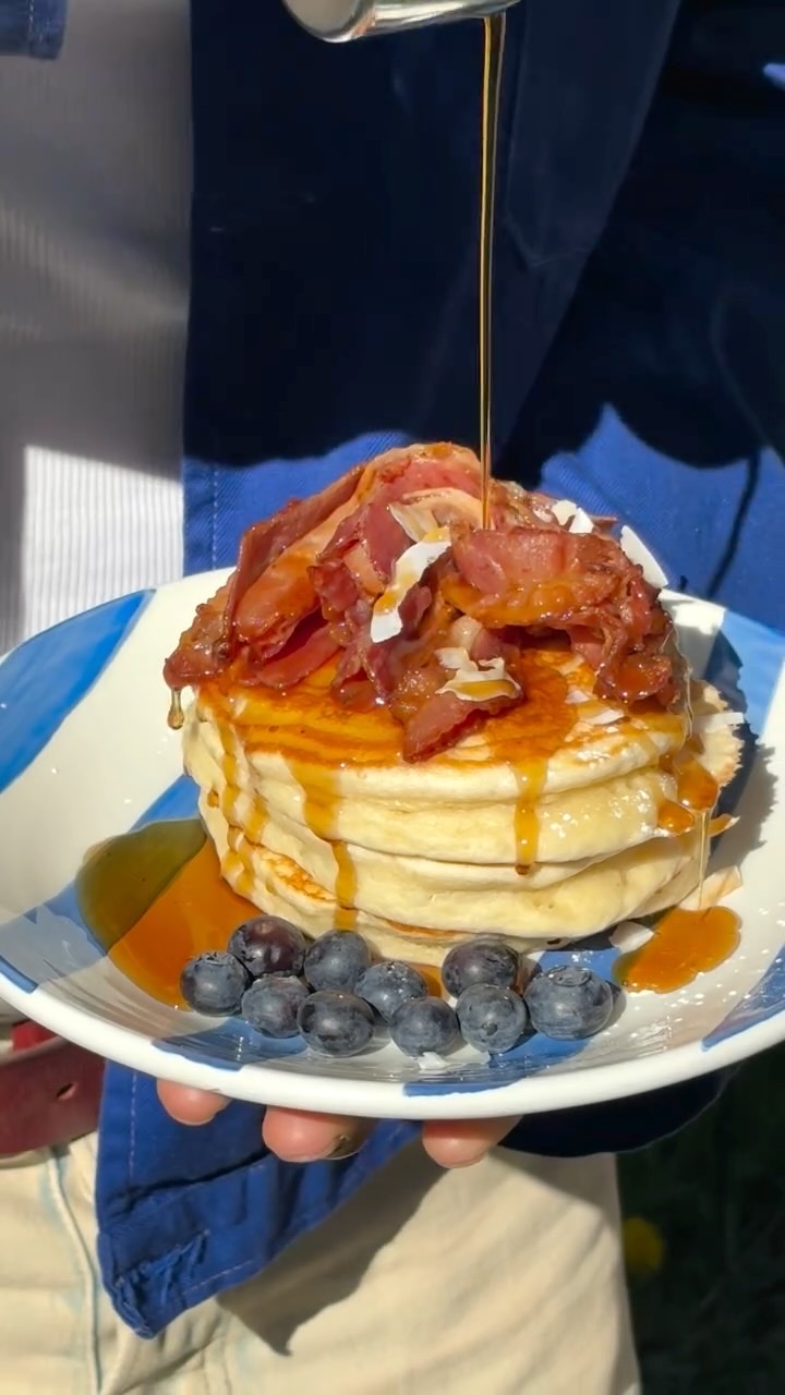 Stapel amerikanska pannkakor med bacon, blåbär och lönnsirap som hälls över