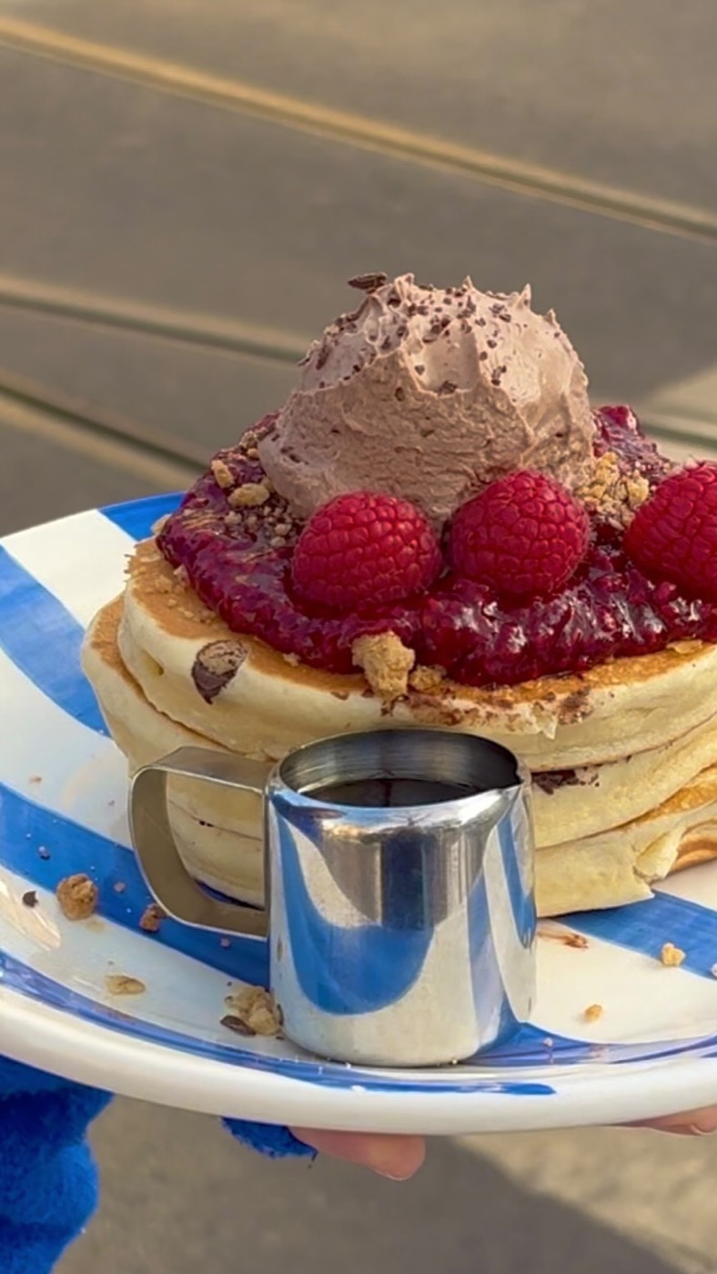 Pannkakor med hallon, bärkompott och chokladgrädde på randig tallrik, sirapskanna framför